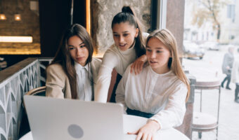 A group of women friends in a cafe are looking at a laptop
