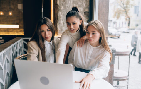 A group of women friends in a cafe are looking at a laptop
