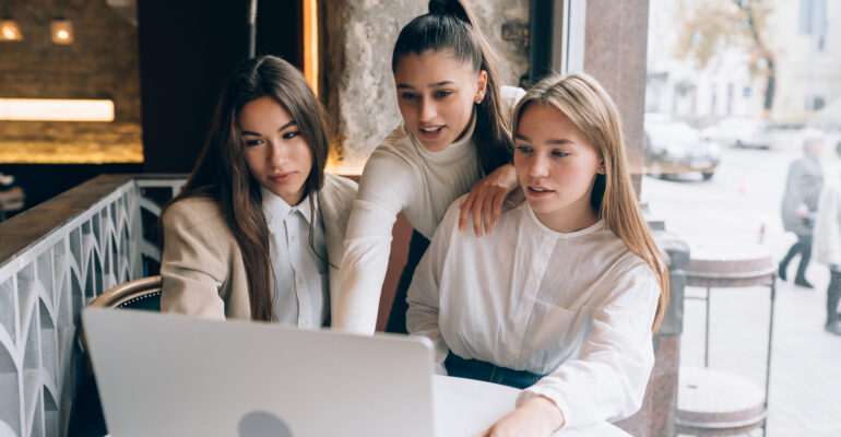 A group of women friends in a cafe are looking at a laptop
